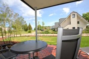 An outdoor patio with a round table and chairs, a covered area, and a view of a residential neighborhood.