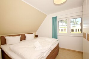 A bedroom with a bed, a nightstand, a window with curtains, and a view of buildings outside. - Beachfront vacation rental with a balcony, access to the pool and sauna - Rex Rugia H-1010 - (Göhren)