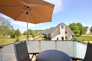 A balcony with a glass balustrade, an outdoor umbrella, and a view of a residential area with houses and trees. - Beachfront vacation rental with a balcony, access to the pool and sauna - Rex Rugia H-1010 - (Göhren)