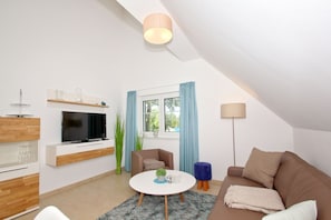 A modern living room with a flat-screen TV, a round coffee table, a brown sofa, and a blue accent chair.