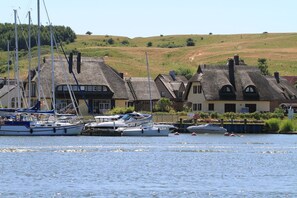 A coastal village with traditional thatched-roof houses, a marina with several boats, and a hilly landscape in the background. - Beachfront vacation rental with a balcony; access to the pool and sauna - Rex Rugia - Rex Rugia (Göhren)
