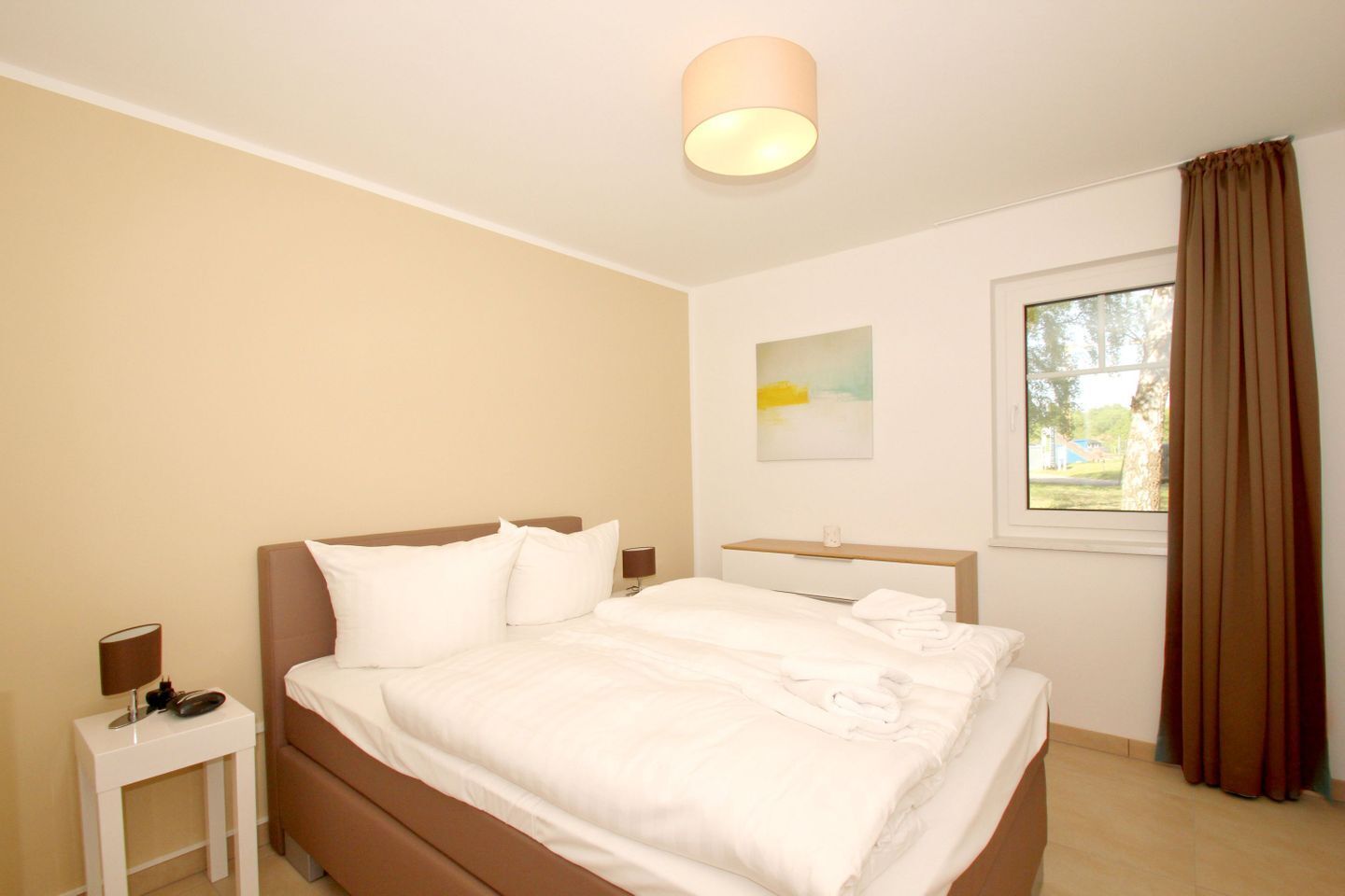 Una habitación de hotel con cama, mesita de noche, lámpara y ventana con cortinas.