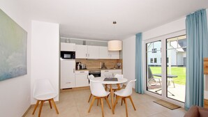 A modern kitchen with white cabinets, a dining area with a white table and chairs, and a large sliding glass door leading to a patio with outdoor furniture. - Beachfront vacation rental with a terrace, access to the pool and sauna - Rex Rugia H-1010 - (Göhren)