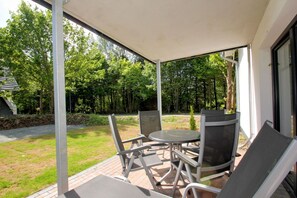 Une terrasse couverte, dotée d’une table et de chaises, qui offre une vue sur une pelouse et des arbres.