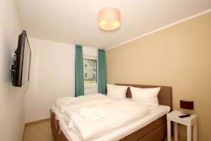 A hotel room with a bed, a bedside table with a lamp, a TV mounted on the wall, and a window with curtains.