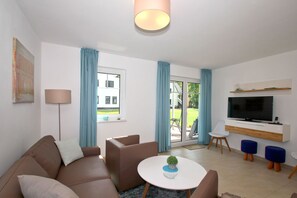 A modern living room with a sofa, a coffee table, a TV, and a sliding glass door leading to a balcony.