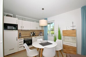 A modern kitchen with white cabinets, a dining table with chairs, and a large window with curtains.