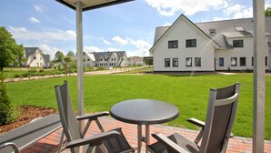 A covered outdoor seating area with a table and chairs, overlooking a well-maintained lawn and a row of houses. - Beachfront vacation rental with a terrace, access to the pool and sauna - Rex Rugia - Rex (Göhren)