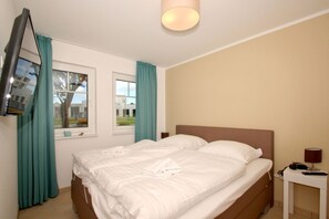 Une chambre d’hôtel avec un lit, un téléviseur fixé au mur, une table de chevet avec une lampe et une fenêtre avec des rideaux.