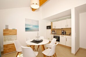 A modern kitchen with white cabinets, a dining area with a round table and white chairs, and a painting on the wall.