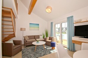 Een moderne woonkamer met een bank, salontafel, televisie en een balkon met gordijnen.