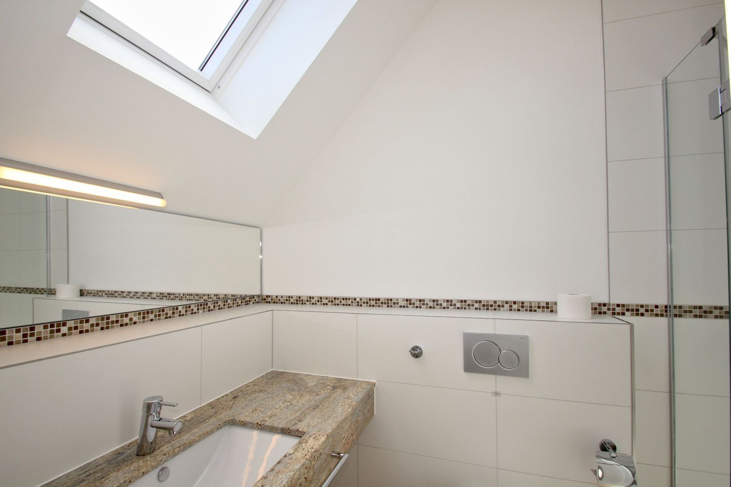 A modern bathroom with a skylight, a granite countertop, a mirror, and a shower area.