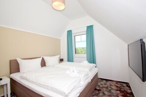 A hotel room with a bed, a TV, a window with curtains, and a ceiling light. - Beachfront vacation rental with a balcony, access to the pool and sauna - Rex Rugia H-1010 - (Göhren)