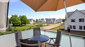 A balcony with a table and chairs, a large umbrella, and a view of houses and greenery. - Beachfront vacation rental with a balcony, access to the pool and sauna - Rex Rugia H-1010 - (Göhren)