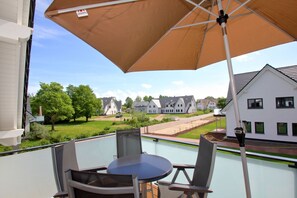 A balcony with a table and chairs, a large umbrella, and a view of houses and greenery. - Beachfront vacation rental with a balcony, access to the pool and sauna - Rex Rugia H-1010 - (Göhren)