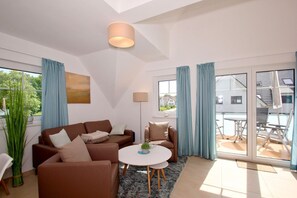 Una sala de estar moderna con sofá, mesa de centro y vista a una casa a través de la puerta de vidrio.