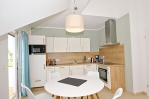 Une cuisine moderne avec des meubles blancs, un plan de travail en bois et un coin repas comprenant une table et des chaises blanches.