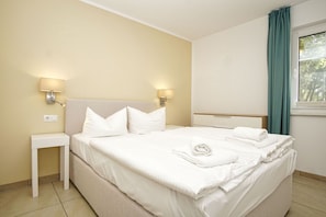 A hotel room with a bed, two bedside lamps, a nightstand, and a window with curtains.