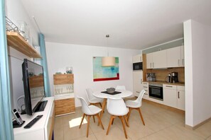 A modern kitchen with white cabinets, a dining table with white chairs, a TV, and a coffee machine. - Beachfront vacation rental with a terrace, access to the pool and sauna - Rex Rugia H-1010 - (Göhren)