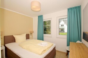 A hotel room with a bed, a desk, a lamp, and a window with curtains. - Beachfront vacation rental with a terrace, access to the pool and sauna - Rex Rugia H-1010 - (Göhren)