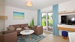 A modern living room with a sofa, coffee table, and a flat-screen TV. - Beachfront vacation rental with a terrace, access to the pool and sauna - Rex Rugia H-1010 - (Göhren)