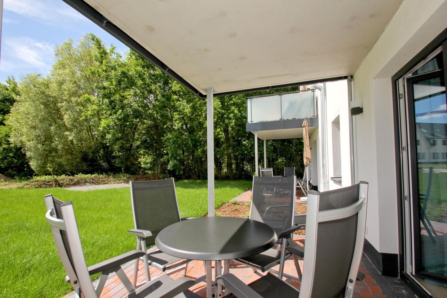 An outdoor patio with a table and chairs, a covered area, and a view of a building and trees.