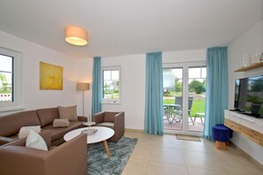 A modern living room with a sofa, coffee table, TV, and a sliding glass door to an outdoor area. - Beachfront vacation rental with a terrace, access to the pool and sauna - Rex Rugia - Rex (Göhren)