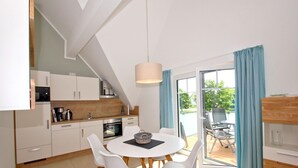 A modern kitchen with white cabinets, a dining table with white chairs, and a view of a garden through large sliding glass doors. - Beachfront vacation rental with a balcony, access to the pool and sauna - Rex Rugia - Rex Rugia (Göhren)