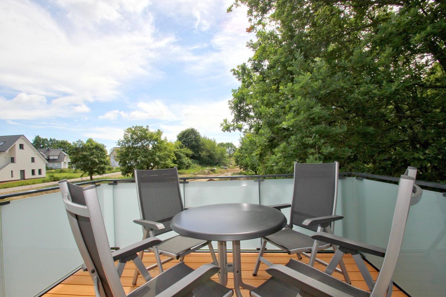 Un balcon doté d’une balustrade en verre, une table ronde et quatre chaises.