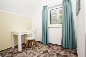 A small room with a white desk, a white chair, a window with teal curtains, and a patterned carpet. - Beachfront apartment with balcony, use of swimming pool and sauna - Rex Rugia H-1010 - (Göhren)