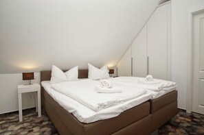 A bedroom with a bed, pillows, a nightstand, and a door. - Beachfront apartment with balcony, use of swimming pool and sauna - Rex Rugia H-1010 - (Göhren)