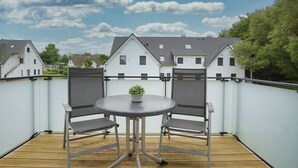 En balkon med et rundt bord og to stole, en lille potteplante og udsigt til huse i baggrunden.