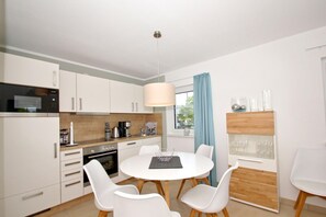 A modern kitchen with white cabinets, a dining table with four chairs, a coffee maker, and a hanging light fixture. - Beachfront vacation rental with a balcony, access to the pool and sauna - Rex Rugia H-1010 - (Göhren)