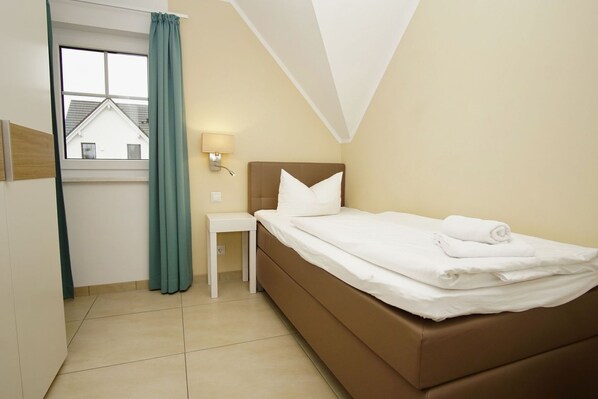 A hotel room with a bed, a nightstand, a lamp, a window with curtains, and a view of a building outside.