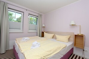 Una cama doble bien hecha con almohadillas, una lámpara de noche y una ventana con cortinas.