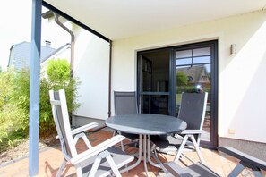 Une terrasse extérieure avec une table ronde et quatre chaises, une porte-fenêtre coulissante et une vue sur un quartier résidentiel.
