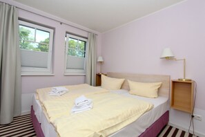 A hotel room with a bed, two windows, a bedside lamp, and a striped floor. - Beachfront vacation rental with a terrace, access to the pool and sauna - Rex Rugia H-1010 - (Göhren)