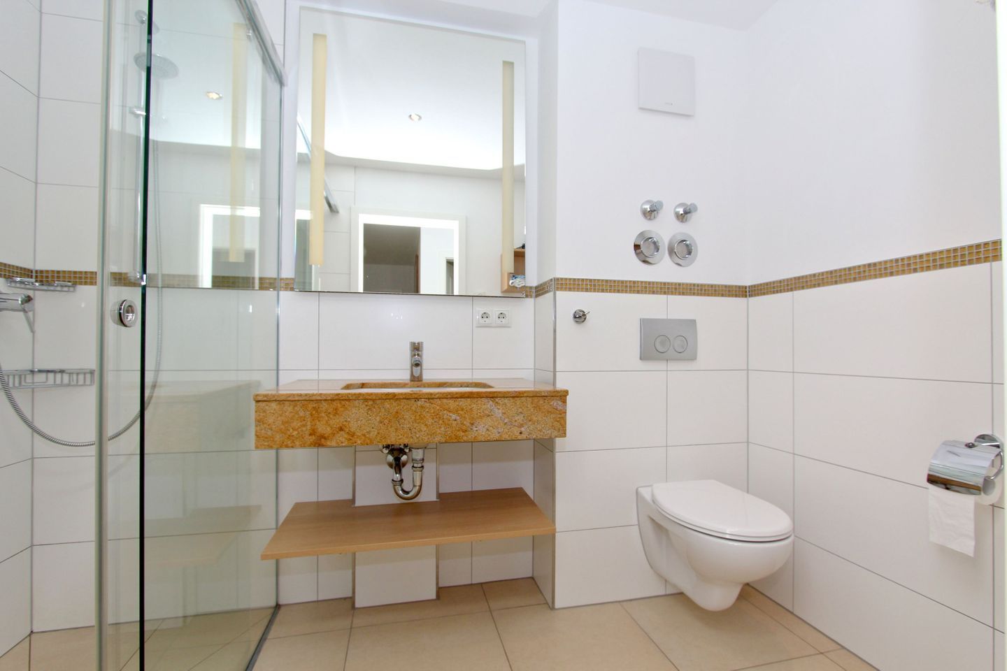 Un baño con cabina de ducha de vidrio, lavamanos con encimera de granito, inodoro blanco y espejo sobre el lavamanos.