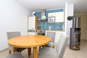 A modern kitchen with a round wooden table, grey upholstered chairs, a built-in microwave, and a wood-burning stove. - Beachfront apartment with a terrace; access to the pool and sauna - Rex Rugia Apartment 28-2 (Göhren)