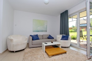 A modern living room with a sofa, two armchairs, a coffee table, and a large window with a view of a garden. - Beachfront apartment with a terrace; access to the pool and sauna - Rex Rugia Apartment 28-2 (Göhren)