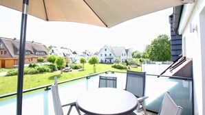 Ein Balkon mit Tisch und Stühlen, einem großen Sonnenschirm und Blick auf Häuser und Grünflächen.