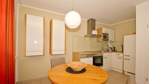 A modern kitchen with a round wooden table, a hanging light fixture, and white cabinets. - Beachfront vacation rental with a terrace, access to the pool and sauna - Rex Rugia H-1010 - (Göhren)