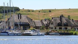 A coastal village with traditional thatched-roof houses, a marina with several boats, and a hilly landscape in the background. - Beachfront vacation rental with a terrace, access to the pool and sauna - Rex Rugia H-1010 - (Göhren)