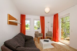 A modern living room with a dark brown sofa, two chairs, a small white table, and a large window with red curtains.