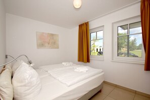 A hotel room with a bed, a window with curtains, a wall-mounted light, and a painting. - Beachfront vacation rental with a terrace, access to the pool and sauna - Rex Rugia H-1010 - (Göhren)