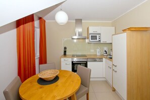 A compact kitchen with a microwave, stove, and dishwasher, a wooden dining table with chairs, and a red curtain.