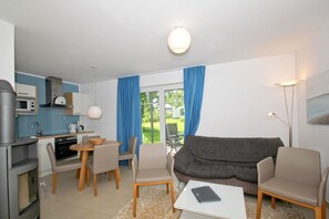 A modern living room with a grey sofa, a dining table with chairs, and a kitchen area with a microwave and stove. - Beachfront vacation rental with a terrace, access to the pool and sauna - Rex Rugia H-1010 - (Göhren)