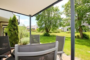 Un patio couvert avec une table et des chaises, entouré de verdure et d’arbres.