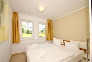 A hotel room with two windows, a bed with white linens, and a headboard. - Beachfront vacation rental with a terrace, access to the pool and sauna - Rex Rugia H-1010 - (Göhren)