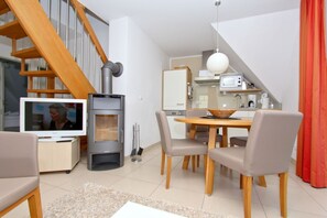 A modern living room with a TV, a fireplace, a dining area with chairs, a kitchen with appliances, and a staircase. - Beachfront vacation rental with a balcony, access to the pool and sauna - Rex Rugia H-1010 - (Göhren)